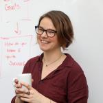 me, in front of a white board with Libby boxes behind me, holding a cup of coffee.